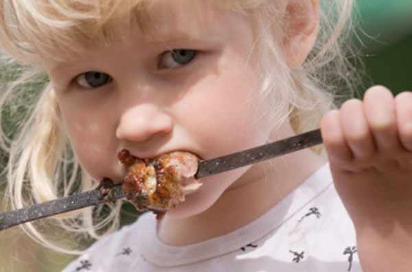 Маленькая девочка кусает мясо с шампура