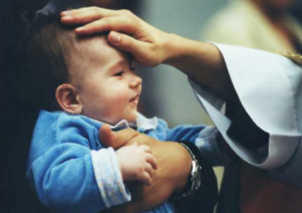 Родители держат ребенка на руках. Священник кладет свою руку малышу на лоб
