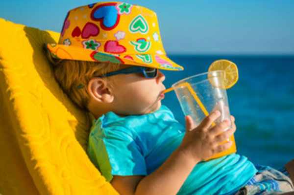 Мальчик в панамке со стаканом сока в руках лежит на кушетке