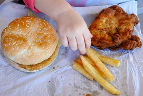 Гамбургер, картошка фри, к которым тянется ручка ребенка