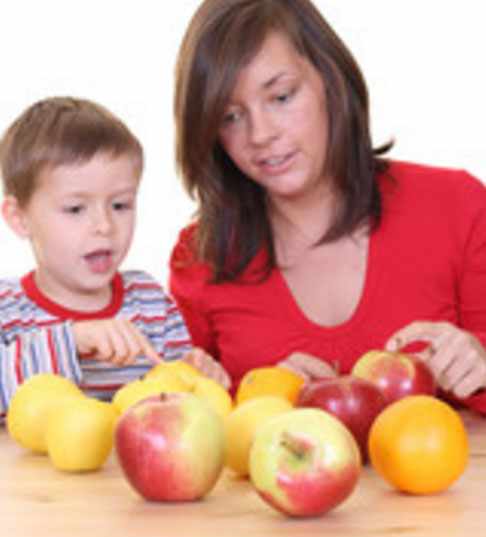 Мальчик сидит с мамой за столом и пересчитывает яблоки