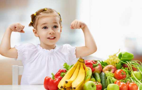 Девочка показывает, какая она сильная. На столе лежат фрукты и овощи