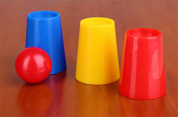 Синий, желтый и красный стаканы, перевернутые вверх ногами, и красный шарик
