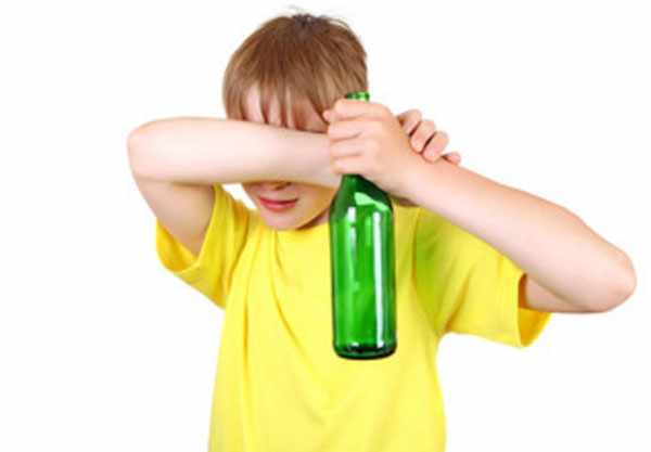 Мальчик с пустой бутылкой от пива в руках прячет свои глаза