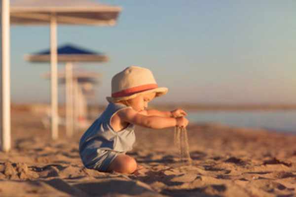 Маленький ребенок играет с песком на морском берегу