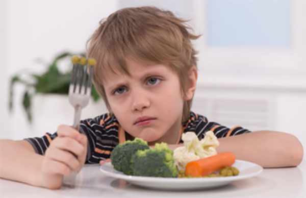 Печальный и бледный ребенок сидит перед тарелкой с овощами