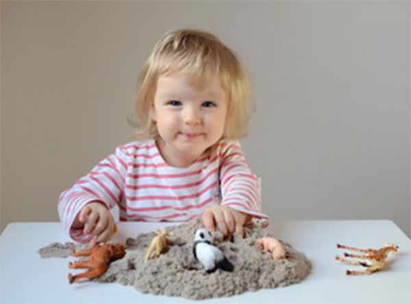 Девочка по песку разложила игрушечных животных