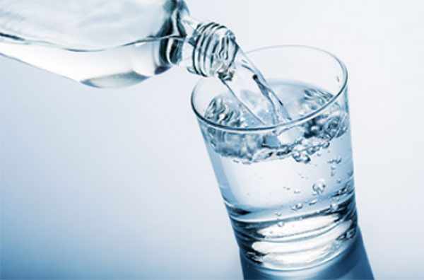 С бутылки наливают воду в стакан