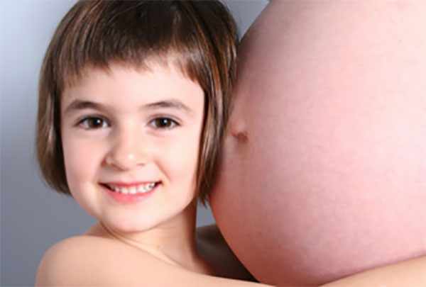 Счастливая девочка прижимается к маминому беременному животу