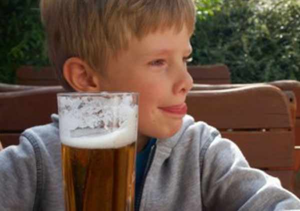Мальчик сидит возле бокала безалкогольного пива и облизывается