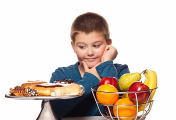 Мальчик смотрит на сладости, рядом емкость с фруктами