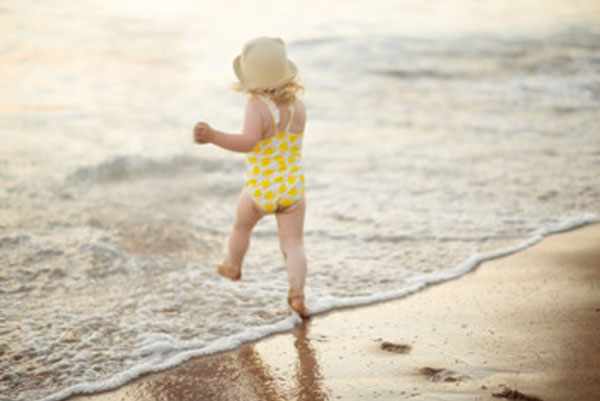 Девочка в панамке и купальнике шагает в морскую воду