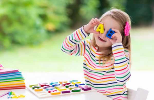 Девочка играет с английскими магнитными литерами, приставляет их к своим глазам. На столе лежит планшетка, на которой остальные литеры
