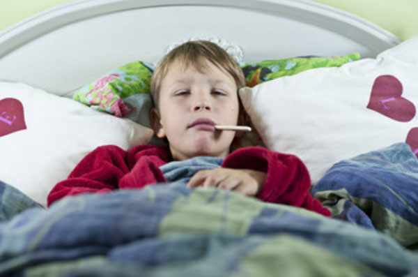 Ребенок лежит в постели с градусником во рту