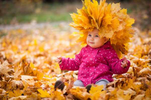 Ребенок сидит в осенней листве. На голове венок из осенних листьев
