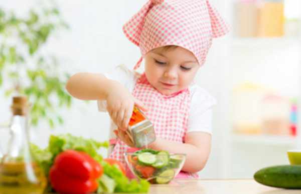 Маленькая девочка в косынке и фартуке готовит овощной салат