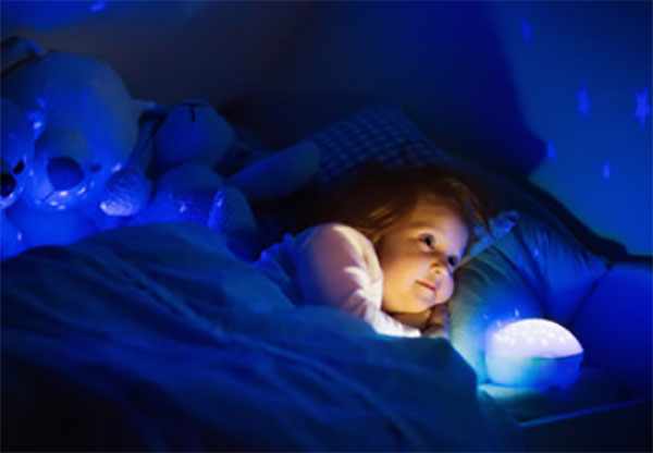 Девочка лежит в кровати, в комнате включенный светильник