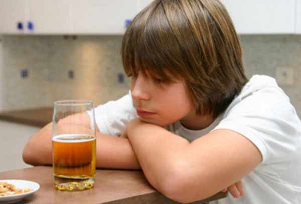 Мальчик сидит за столом. Перед ним стоит бокал пива, он на него томно смотрит