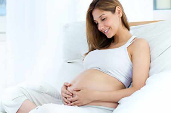 Беременная женщина сидит на кровати и обнимает свой живот