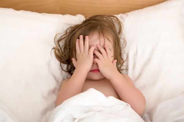 Ребенок лежит в постели, закрывает лицо руками