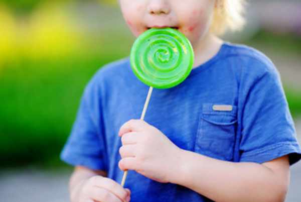 Ребенок облизывает конфету на палочке. У него сыпь на лице