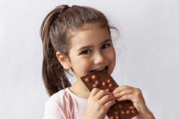Девочка кусает плитку шоколада с орехами