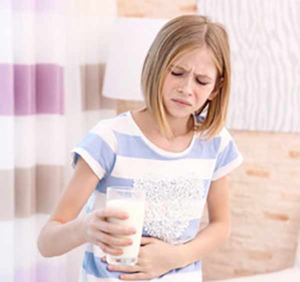 Девочка со стаканом молока держится за живот и корчится от неприятных ощущений