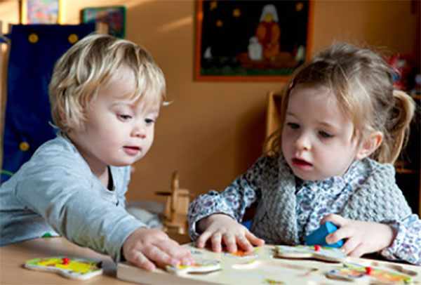 Два ребенка сидят за столом, вместе играют развивающей игрой