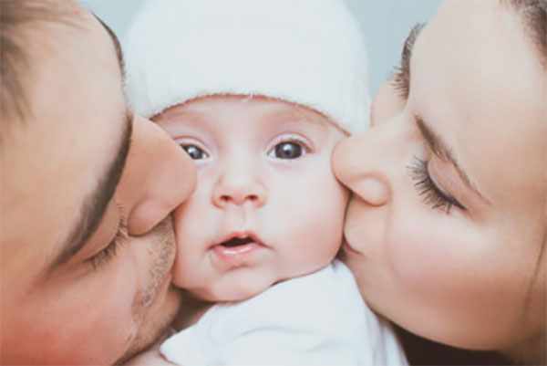 Мама и папа с двух сторон целуют щечки крохотного сыночка