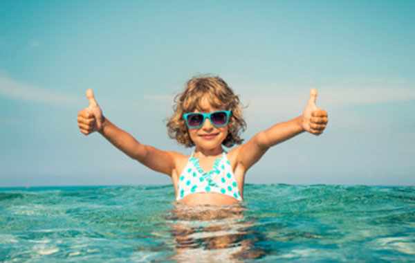 счастливая девочка в солнцезащитных очках на море. стоит в воде
