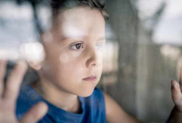Мальчик с грустным лицом стоит у окна