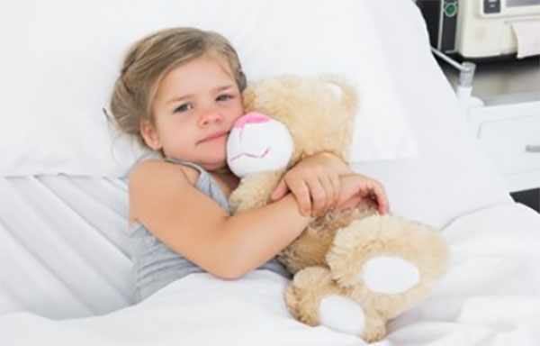Девочка лежит в постели и обнимает плюшевого медведя