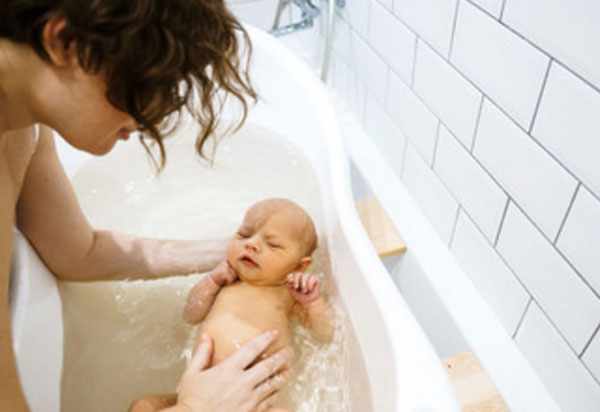 Мама купает грудного ребенка в детской ванночке