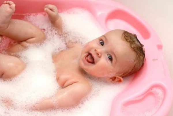 Ребенок смеется, лежа в ванночке