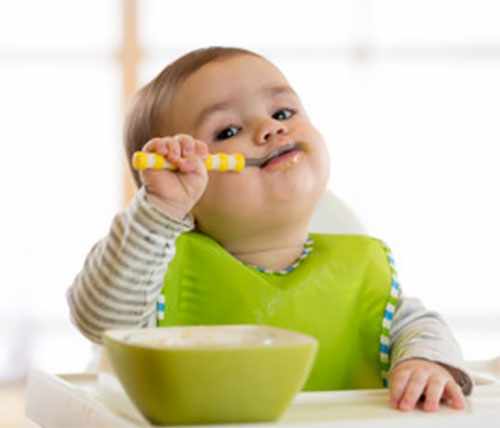 Ребенок в слюнявчике самостоятельно кушает