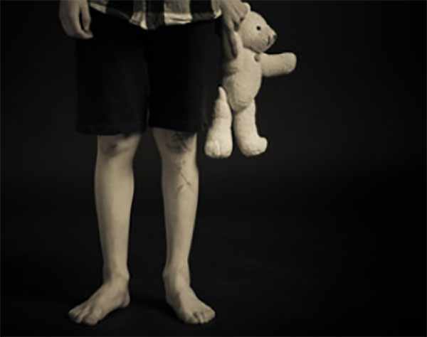 Ноги мальчика с игрушкой в руках. Стоит в темноте