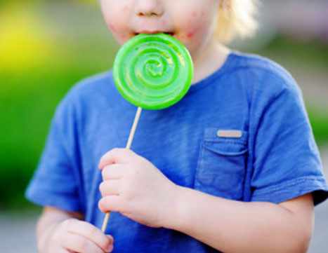 Ребенок с сыпью на щеках ест большую конфету на палочке