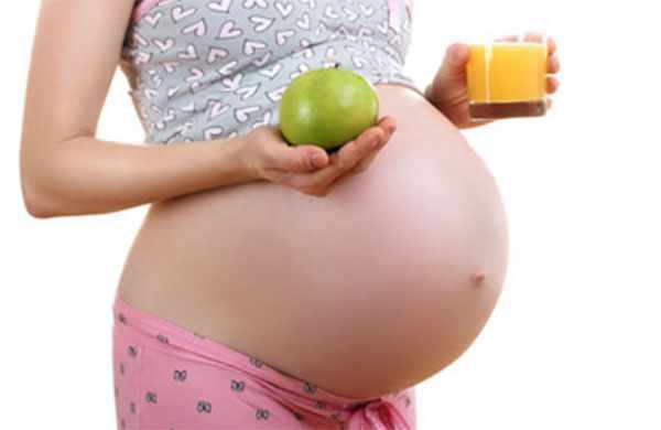 Беременная женщина держит стакан с соком и зеленое яблоко