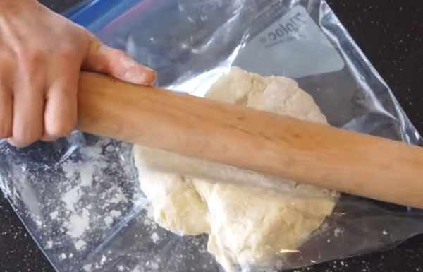 Скалкой разминают тесто в пакете