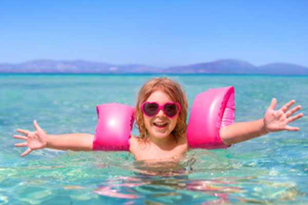 Счастливая девочка в воде с нарукавниками и в солнцезащитных очках