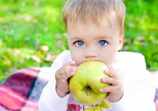 Ребенок кусает зеленое яблоко