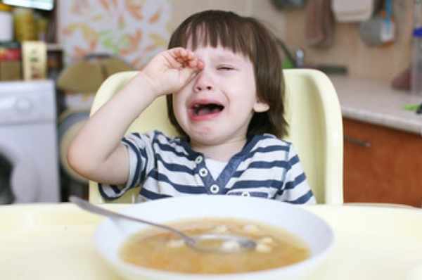 Ребенок плачет. Перед ним стоит тарелка с едой