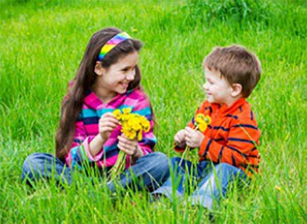 Девочка и мальчик помладше сидят на траве с цветами в руках и разговаривают
