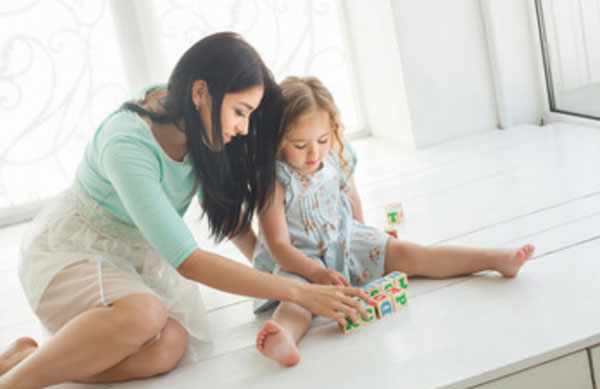 Мама с дочкой сидят на полу и собирают слова на английском при помощи кубиков, на которых изображены английские литеры