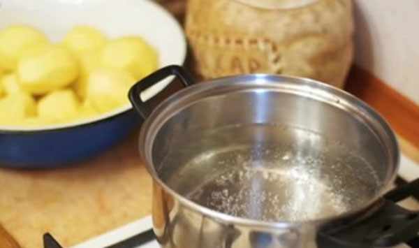 Закипает вода в кастрюле. на заднем плане в миске очищенная картошка