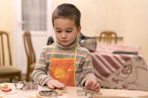 Мальчик в фартуке стоит у стола, на котором лежат его изделия