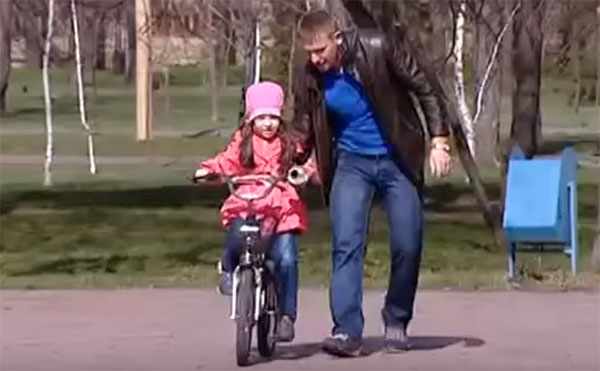 Папа учит ребенка кататься на двухколесном велосипеде